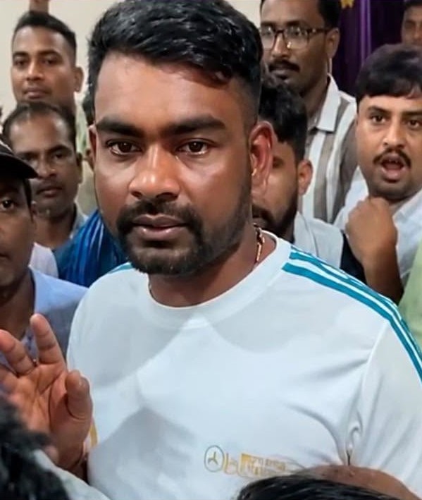 सफेद टी-शर्ट पहने एक व्यक्ति भीड़ में खड़ा है और अपना हाथ उठाए हुए है।