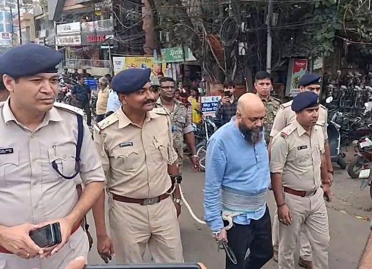 पुलिस अधिकारी एक व्यक्ति को हिरासत में लेकर सड़क पर ले जा रहे हैं।