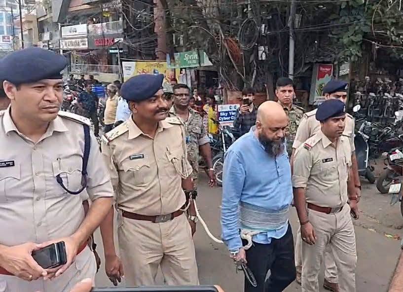 पुलिस अधिकारी एक व्यक्ति को हिरासत में लेकर सड़क पर ले जा रहे हैं।