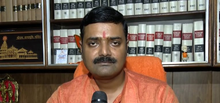 राकेश त्रिपाठी एक पुस्तकालय के सामने बैठे हैं, जिसके पीछे सुप्रीम कोर्ट के मामलों की किताबें रखी हैं।