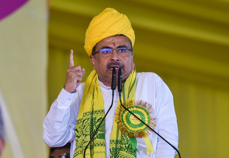 पीली पगड़ी और दुपट्टा पहने एक व्यक्ति मंच पर माइक्रोफोन के सामने भाषण देते हुए अपनी उंगली ऊपर उठाए हुए हैं।