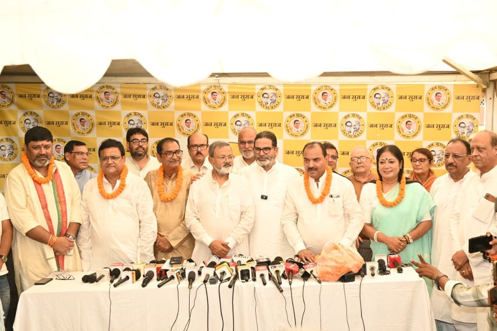 जन सुराज के बैनर के सामने खड़े कई लोग एक प्रेस कॉन्फ्रेंस को संबोधित कर रहे हैं।